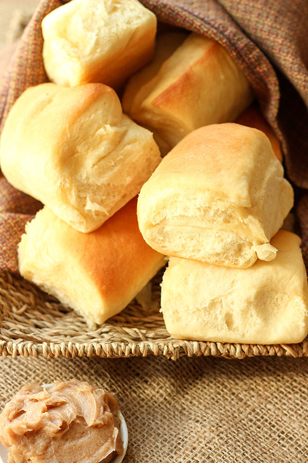 A basket is loaded up with big golden copycat Texas Roadhouse Rolls. Next to the rolls is a dish of cinnamon honey butter.