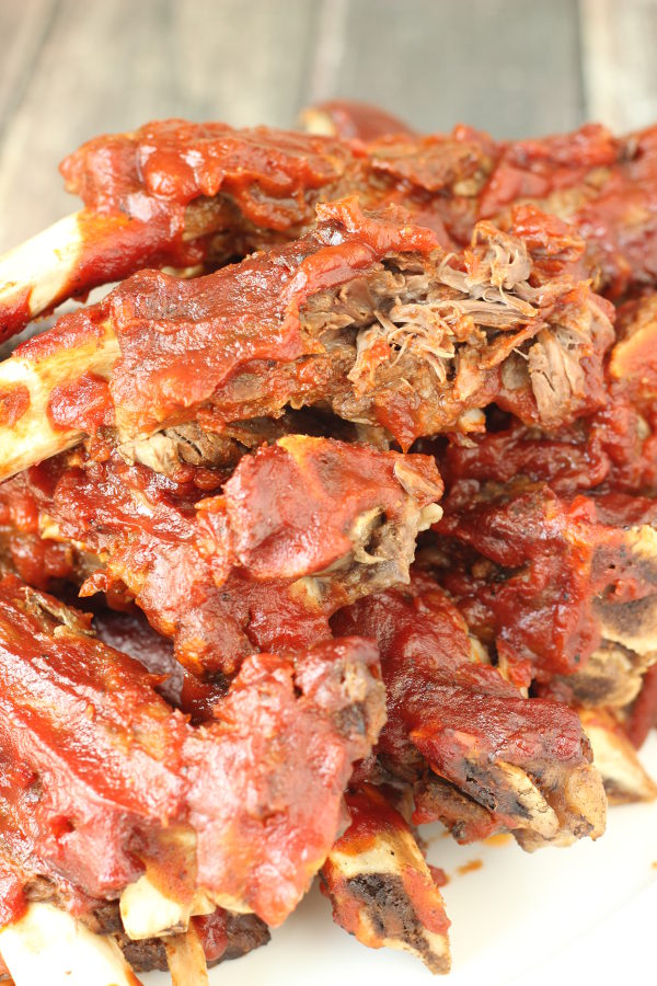 A big pile of bbq beef ribs is stacked up on a plate. The ribs are covered in a spicy red sauce.