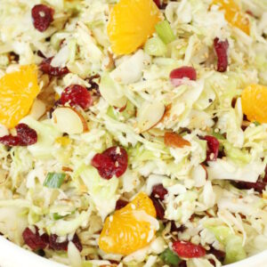 A big white bowl full of Asian coleslaw. You can see dried cranberries and mandarin oranges tucked in the shredded cabbage