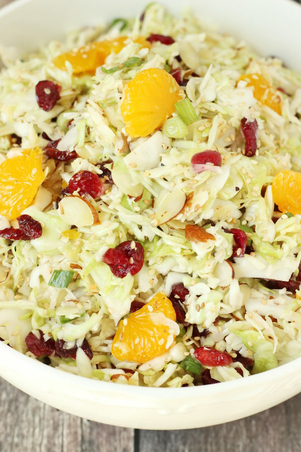 A big white bowl full of Asian coleslaw. You can see dried cranberries and mandarin oranges tucked in the shredded cabbage