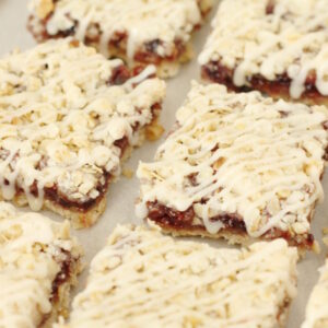 Berry crumb bars are laid out in two rows. The bars are square and have a crumb topping and icing drizzle.