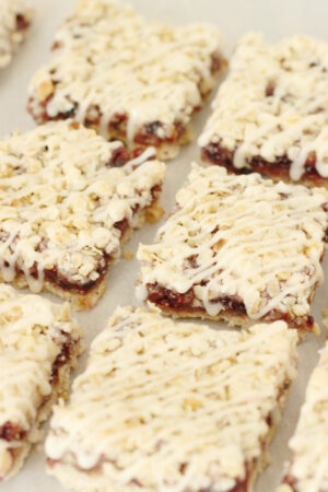 Berry crumb bars are laid out in two rows. The bars are square and have a crumb topping and icing drizzle.