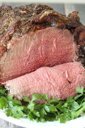 This is a perfectly roasted medium-rare beef roast on a bed of parsley and white plate.