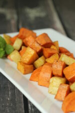 A white platter of roasted yams and sweet potatoes dusted with cinnamon. This healthy side dish looks appitizing.