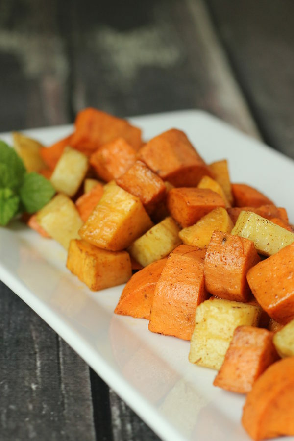 A white platter of roasted yams and sweet potatoes dusted with cinnamon.  This healthy side dish looks appitizing.