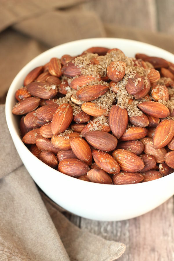 A big white bowl is full of fried almonds. You can see plenty of gray, smoked sea salt on the nuts. 