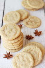Lovely anise cookies are stacked and scattered over a white table. Some whole pods of anise are visible in the photo.