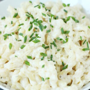 A large white bowl is full of creamy one pot pasta made with boursin cheese. Minced chives garnish the pasta.