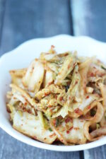 A white bowl of homemade kimchi. You can see slices of napa cabbage and the Korean red pepper flakes on the kimchi.