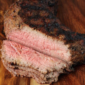A cutting board has a grilled tri tip with slices off of one end.