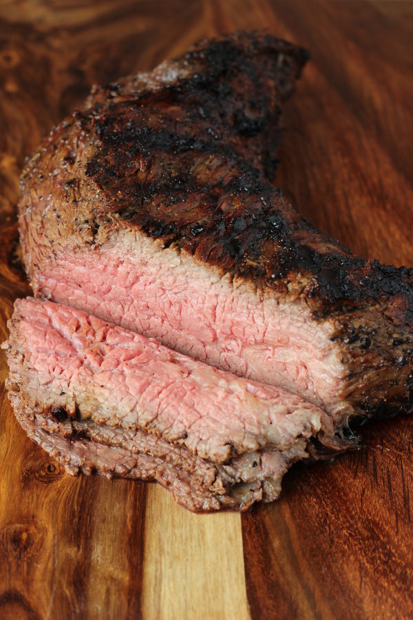 A cutting board has a grilled tri tip with slices off of one end.