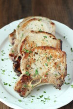 a large white platter has four big pork chops on it. Each chop is perfectly golden. There is a sprinkling of parsley on top.
