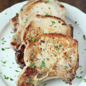 a large white platter has four big pork chops on it. Each chop is perfectly golden. There is a sprinkling of parsley on top.