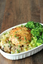A white dish is full of creamy chicken and rice casserole. You can see bites of mushrooms and celery in the rice. There is a side of broccoli on the dish.
