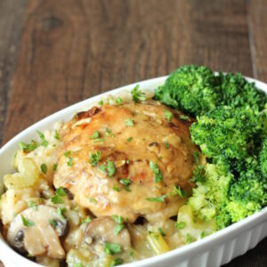 A white dish is full of creamy chicken and rice casserole. You can see bites of mushrooms and celery in the rice. There is a side of broccoli on the dish.