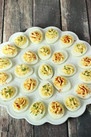 A large deviled egg tray full of classic deviled eggs. The platter is white. The eggs are garnished with paprika or chives.