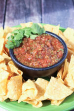 A bowl of 5 minute resturant salsa sits surrounded by chips. The bowl is garnished with cilantro