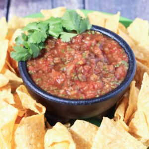 A bowl of 5 minute resturant salsa sits surrounded by chips. The bowl is garnished with cilantro