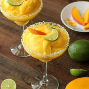 These frosty margarita glasses are full of frozen mango margarita and garnished with fresh mango and lime.