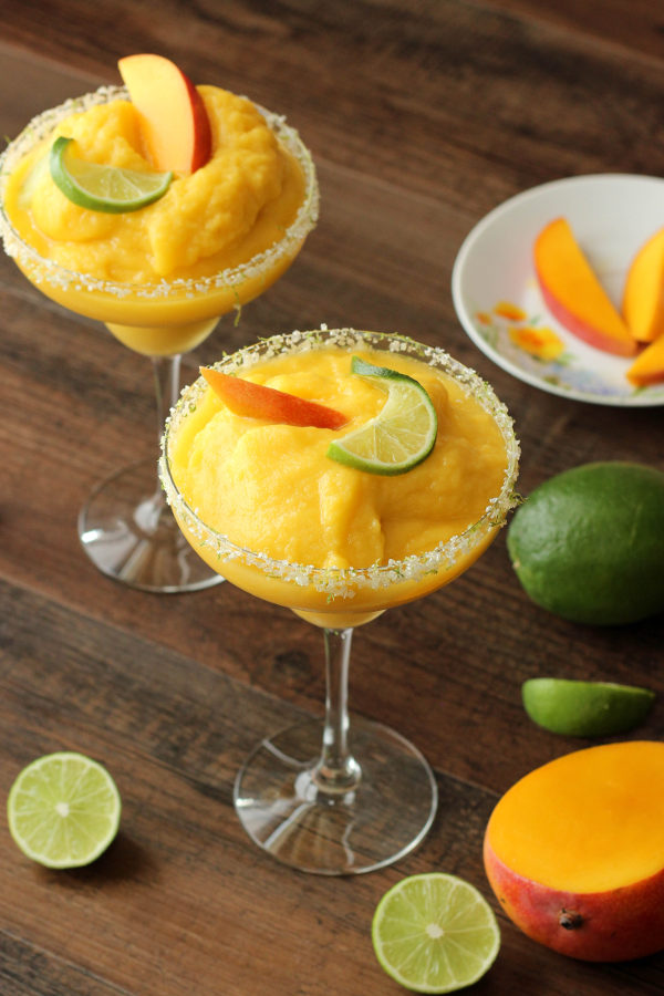 These frosty margarita glasses are full of frozen mango margarita and garnished with fresh mango and lime.