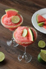 Two frosty glasses of frozen watermelon margaritas garnished with wedges of watermelon and slices of lime.