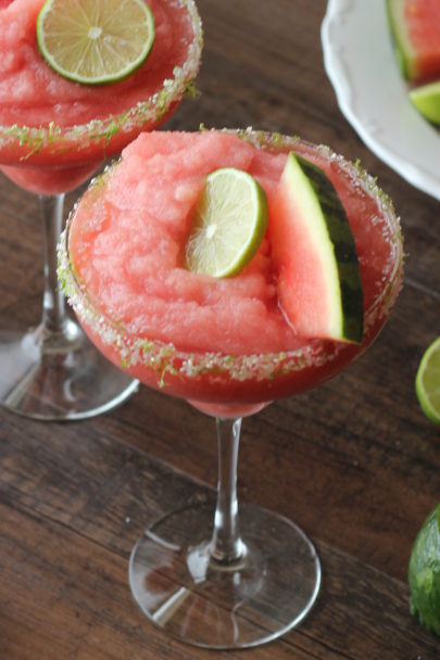 a big chilly glass of frozen watermelon margarita garnished with lime and a watermelon wedge