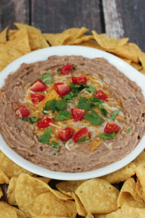 These creamy, flavorful refried beans were made in the instant pot without soaking! They are in a white bowl garnished with tomatoes, cilantro, and cheese. There are chips around the bowl.