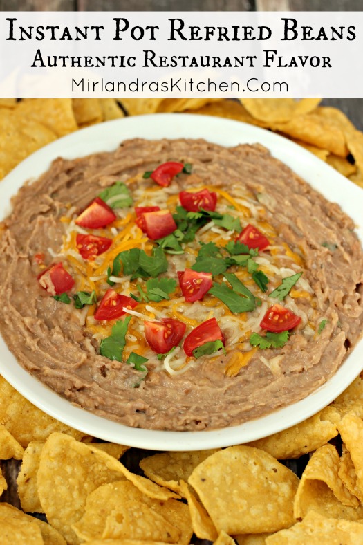 A bowl of refried beans is surrounded by chips and garnished with chunks of tomatoes, cilantro and a sprinkling of cheese.