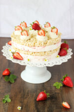 This strawberry ice cream sandwich cake is made from layers of rice crispy treats and strawberry cheesecake ice cream. The cake is decorated with swirls of whipped cream and fresh strawberries.