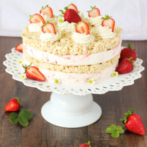 This strawberry ice cream sandwich cake is made from layers of rice crispy treats and strawberry cheesecake ice cream. The cake is decorated with swirls of whipped cream and fresh strawberries.