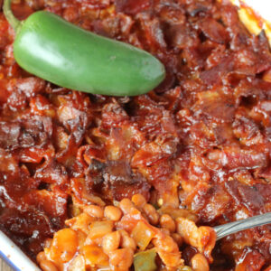 A white and blue pan is full of baked beans. The beans are covered in chopped bacon and the dish has a jalapeno on top.