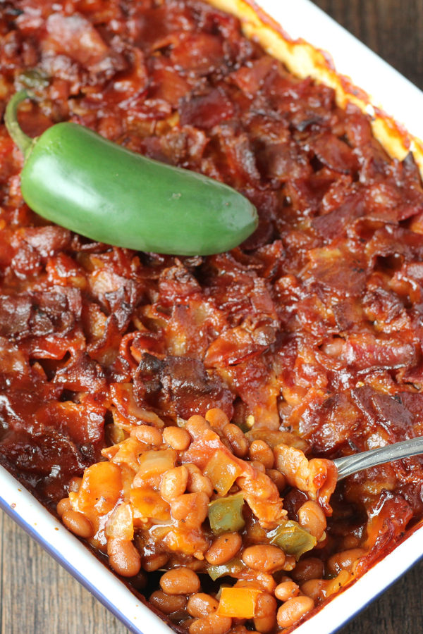 A white and blue pan is full of baked beans. The beans are covered in chopped bacon and the dish has a jalapeno on top.