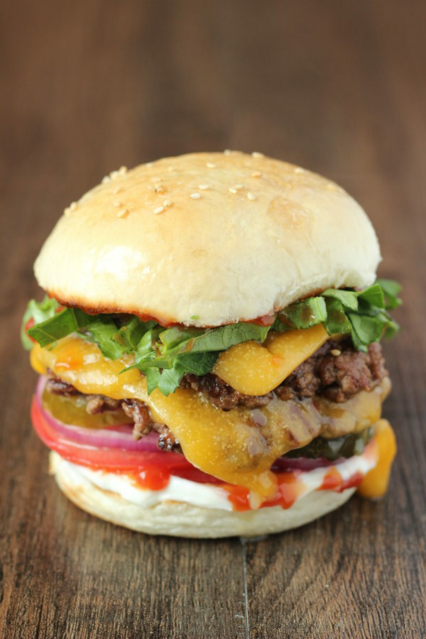 One smashburger with a double patty and mealted cheese. There is lettuce, purple onion, tomato, ketchup and mayo on the burger. 