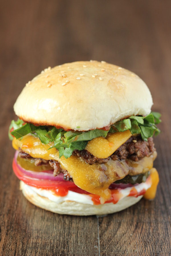 One smashburger with a double patty and mealted cheese. There is lettuce, purple onion, tomato, ketchup and mayo on the burger.