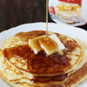 A plate of pancakes is covered in rich syrup that has been modified to taste homemade. You can see the store bought bottle of syrup in the background.