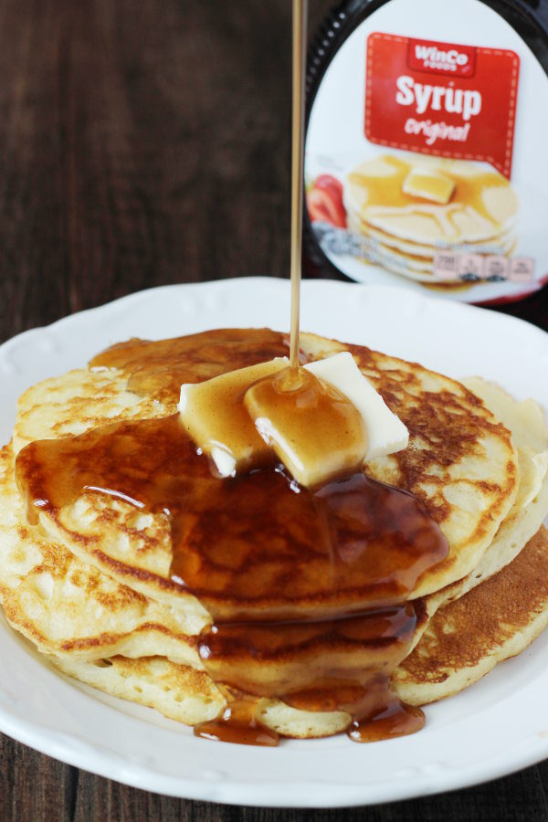 A plate of pancakes is covered in rich syrup that has been modified to taste homemade. You can see the store bought bottle of syrup in the background.