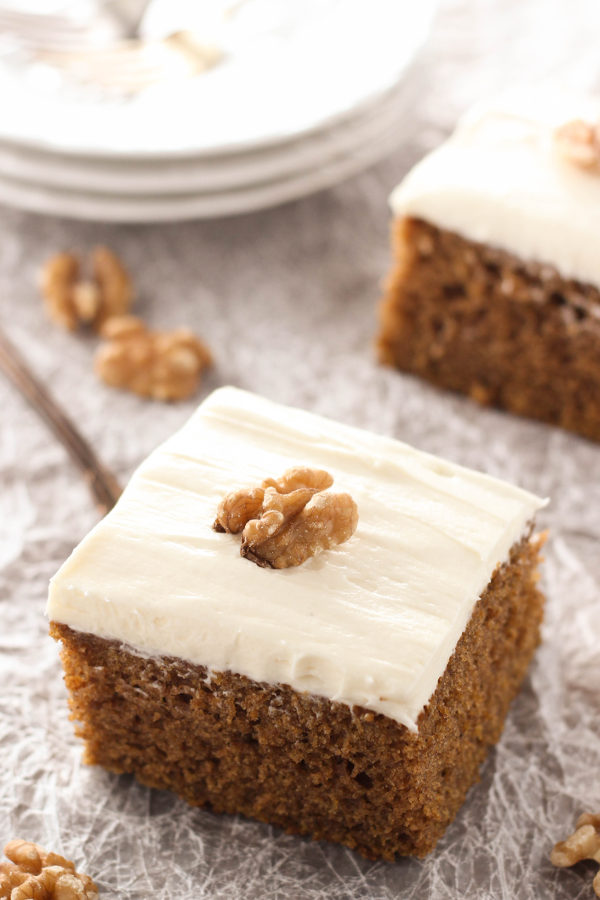 Squares of sweet, spicy pumpkin cake sit ready to eat. The cake is frosted with cream cheese frosting and decorated with walnuts.