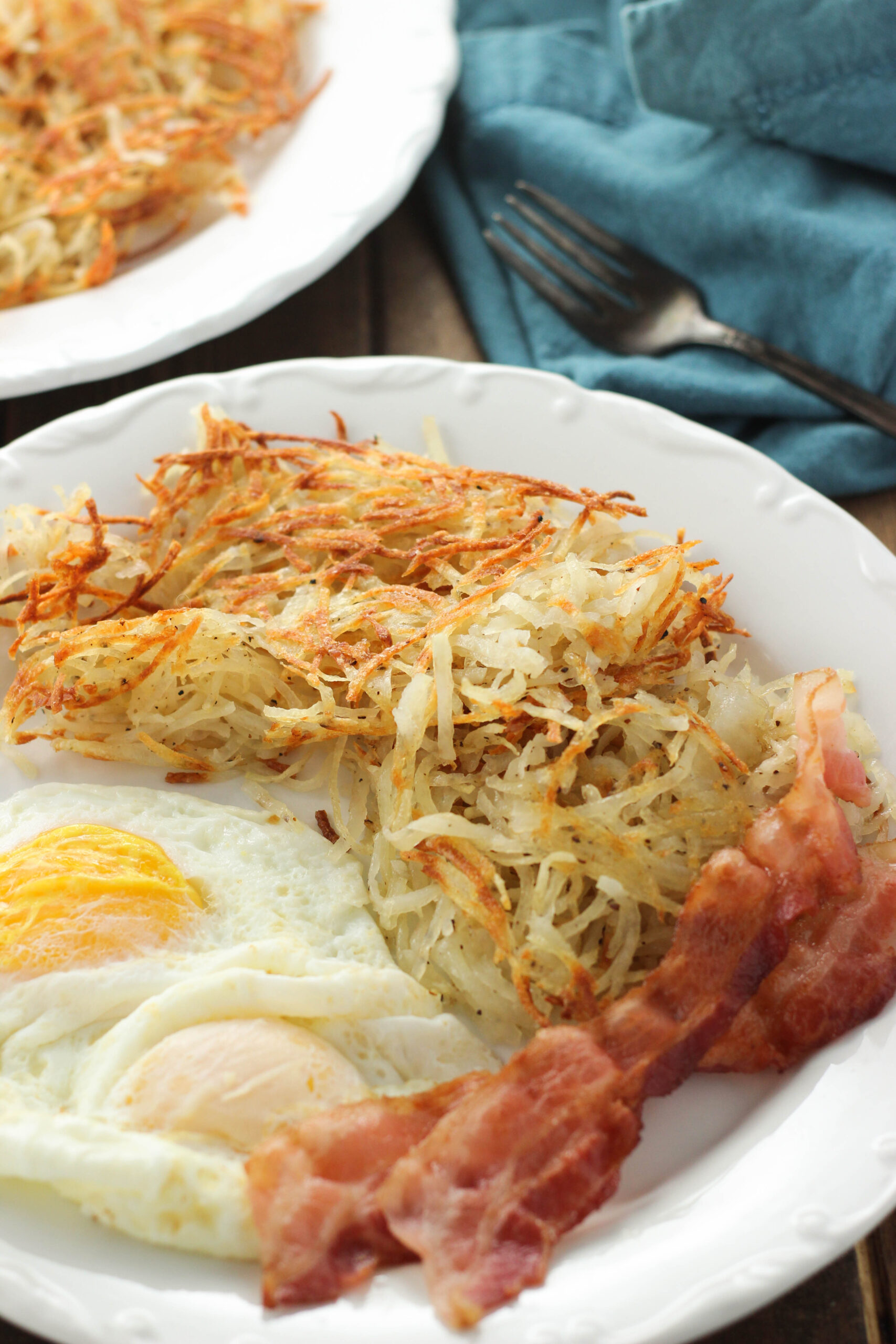 a plate of crispy oven hash browns with over easy eggs and two strips of bacon.