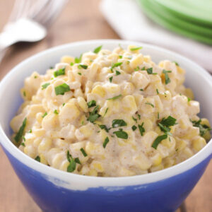 A big creamy helping of slow cooker creamed corn is served in an blue Pyrex bowl. It is garnished with parsley.