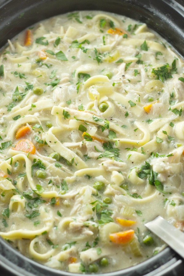 A large crock pot of creamy chicken noodle soup.  You can see egg noodles, carrots, and parsely.