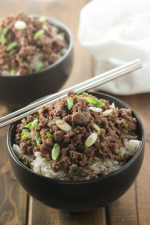 A black bowl is full of rice and then topped with savory Korean ground beef. It is garnished with green onions.
