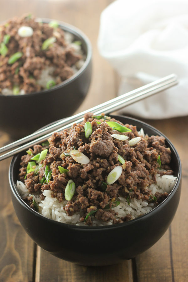 A black bowl is full of rice and then topped with savory Korean ground beef. It is garnished with green onions. 