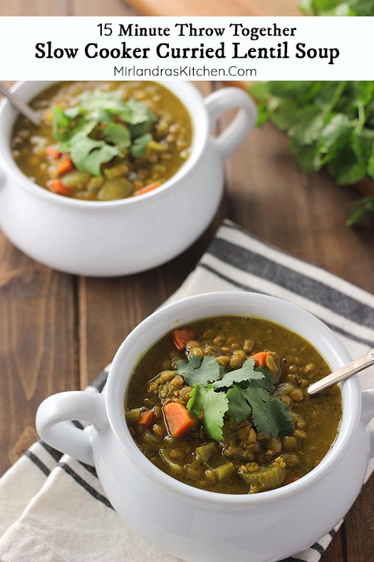 Two bowls of curried lentil soup sit on a wooden table. They are garnished with cilantro.