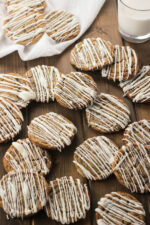 Soft ginger cookies with icing drizzled on them are arranged over a wooden table. There is a glass of milk in the background.