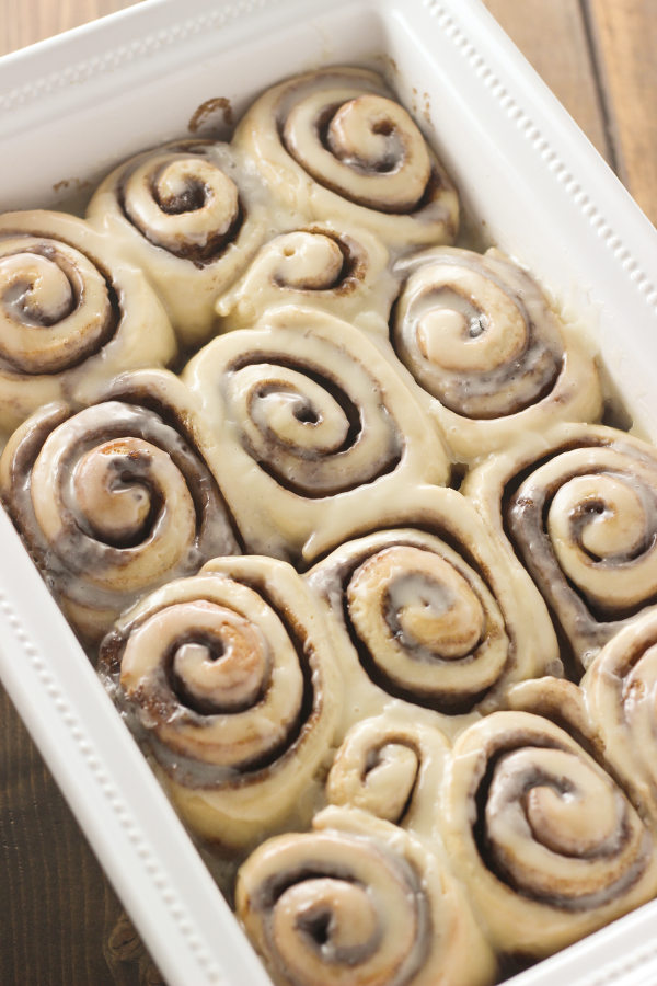 A large white baking dish full of cinnamon rolls slathered in glaze. You can see lots of cinnamon and plenty of sticky glaze.