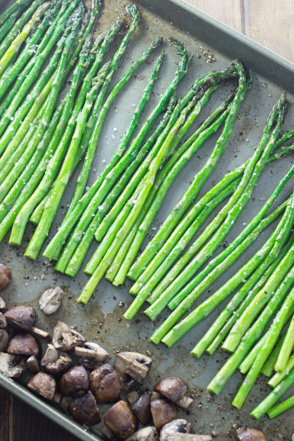 A baking sheet is covered with tender green spears of roasted asparagus and quartered mushrooms.