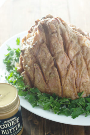 A large diamond cut ham sits on a platter of parsley. The ham has been glazed in cookie butter.