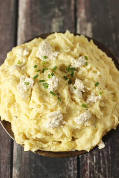 this image features a large pottery bowl full of creamy, Yukon Gold mashed potatoes topped with chunks of tasty Boursin Cheese.