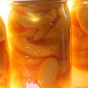 A beautiful jar of home canned peaches sits in front of the light, glowing golden.
