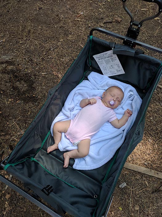 Baby Ella sleeping on a blanket in a wagon on a camping trip.